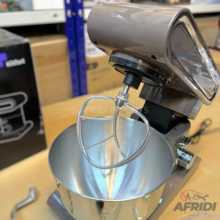 A modern, taupe-colored stand mixer with a stainless steel bowl and a wire whisk attachment.