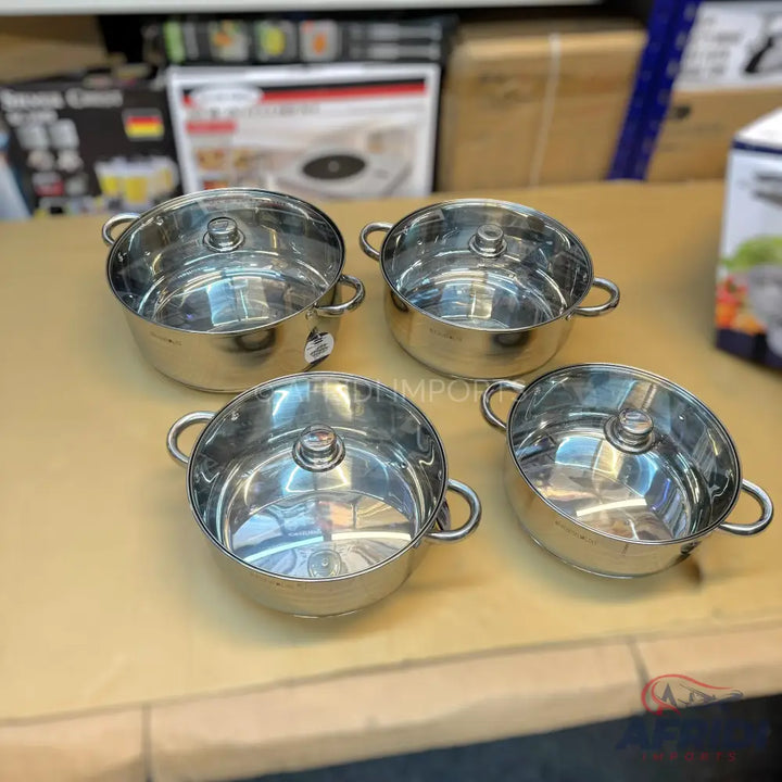 Set of four shiny stainless steel cooking pots with clear glass lids and side handles.