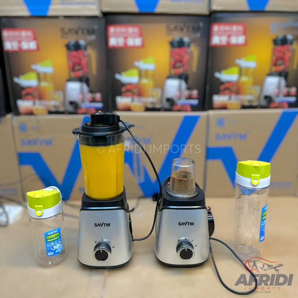 Two blenders, one with a tall pitcher of yellow liquid and the other with a smaller grinder cup containing brown grounds, accompanied by two empty clear plastic bottles with colorful lids.