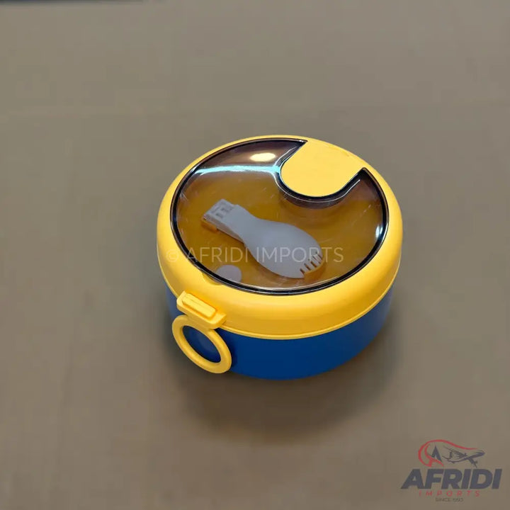 A round, two-tiered lunchbox with a yellow lid, a blue base, and a clear top compartment containing a white spoon and fork.