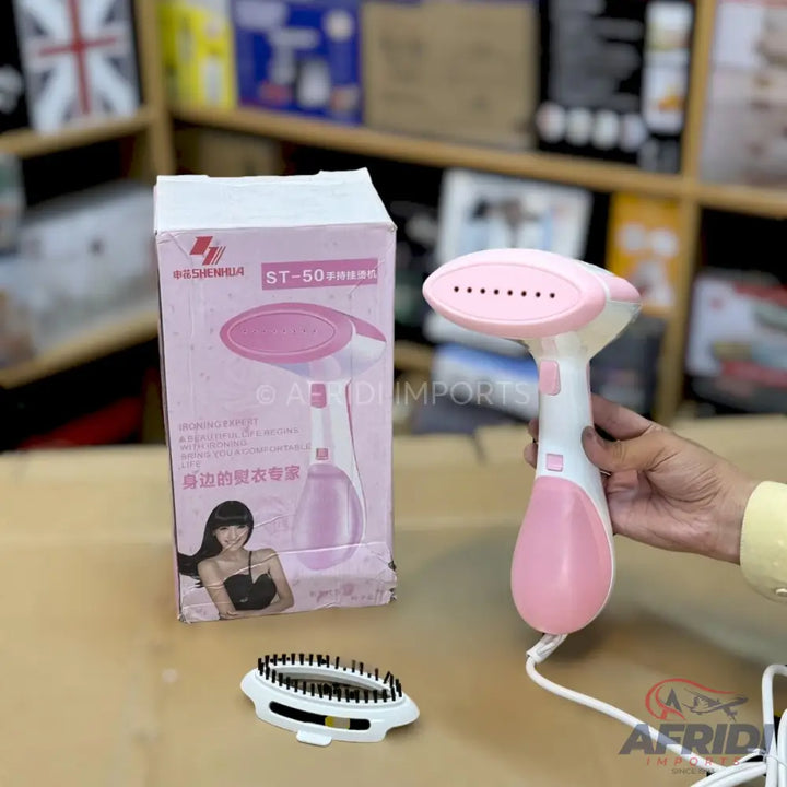 Pink and white handheld garment steamer with an attached brush accessory.