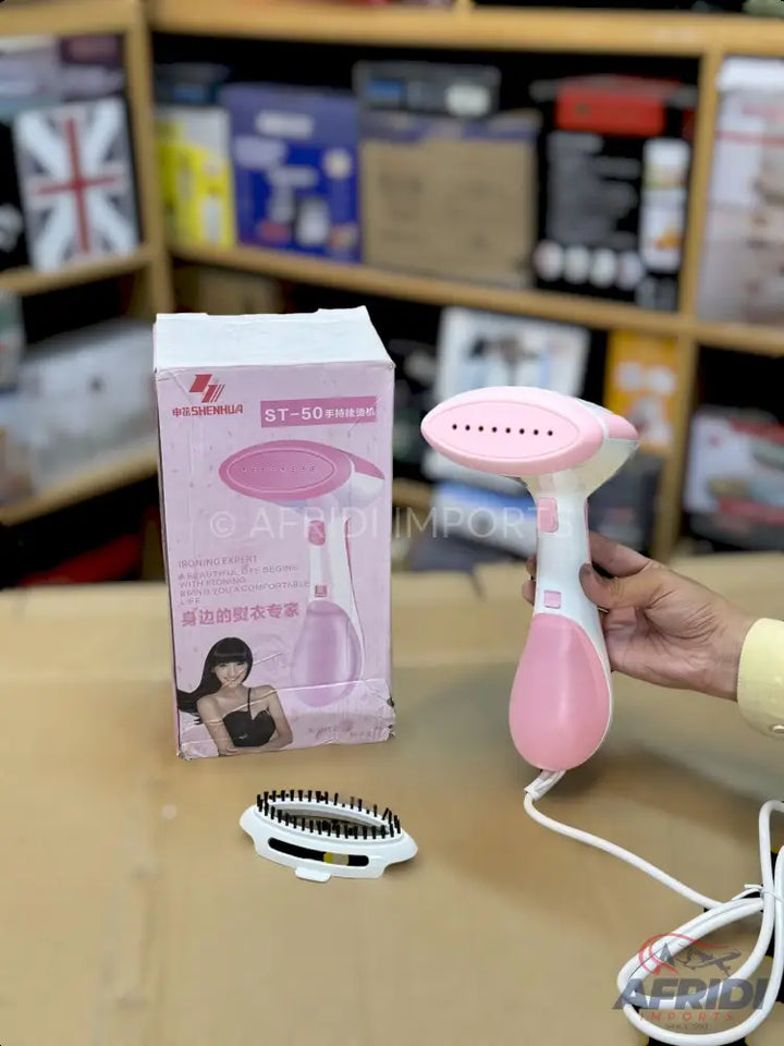 Pink and white handheld garment steamer with a brush attachment.