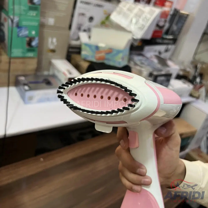 Handheld pink and white garment steamer with a brush attachment.