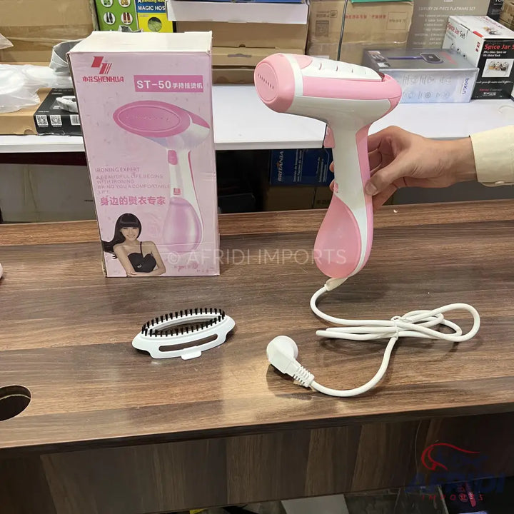 Pink and white handheld garment steamer with included brush attachment.