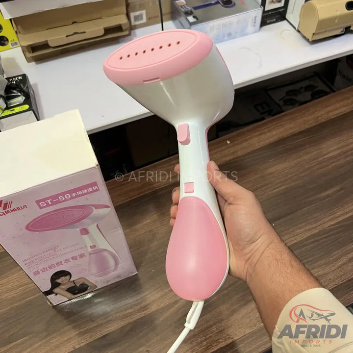 Pink and white handheld garment steamer with a white power cord.