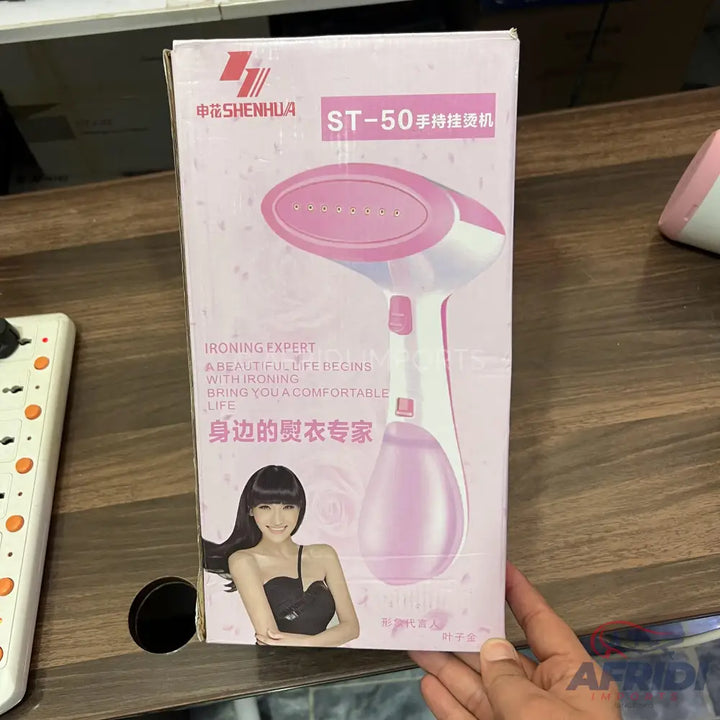 Pink and white handheld garment steamer in its retail packaging.