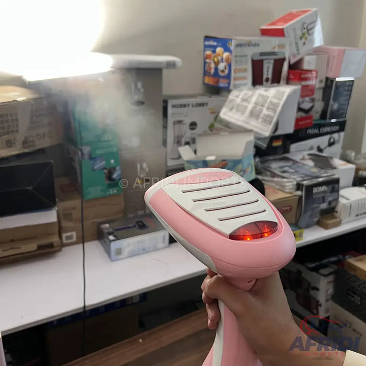 Pink handheld garment steamer with a white top and two glowing red indicator lights.