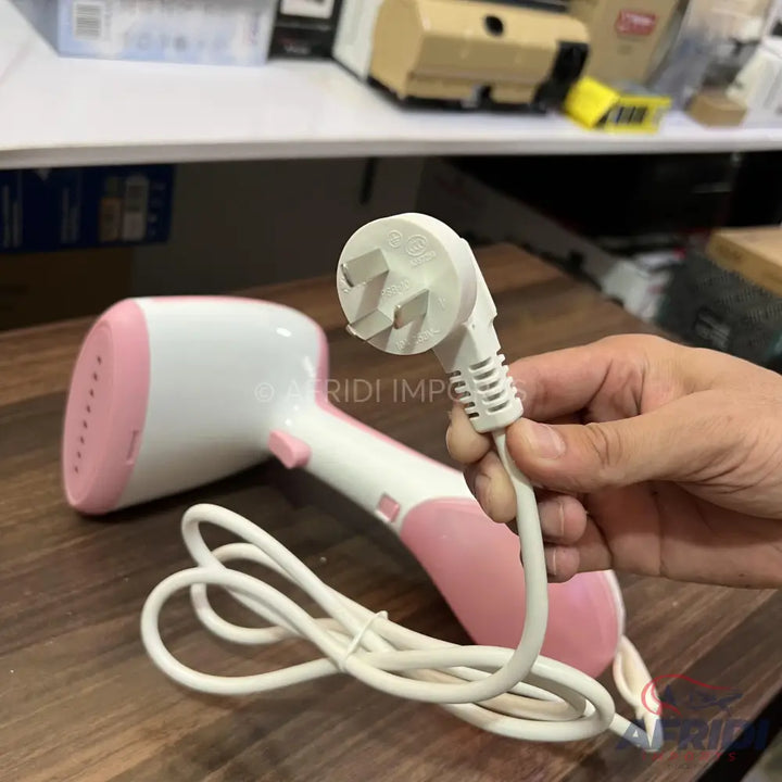Pink and white handheld garment steamer with a UK-style three-pin plug.