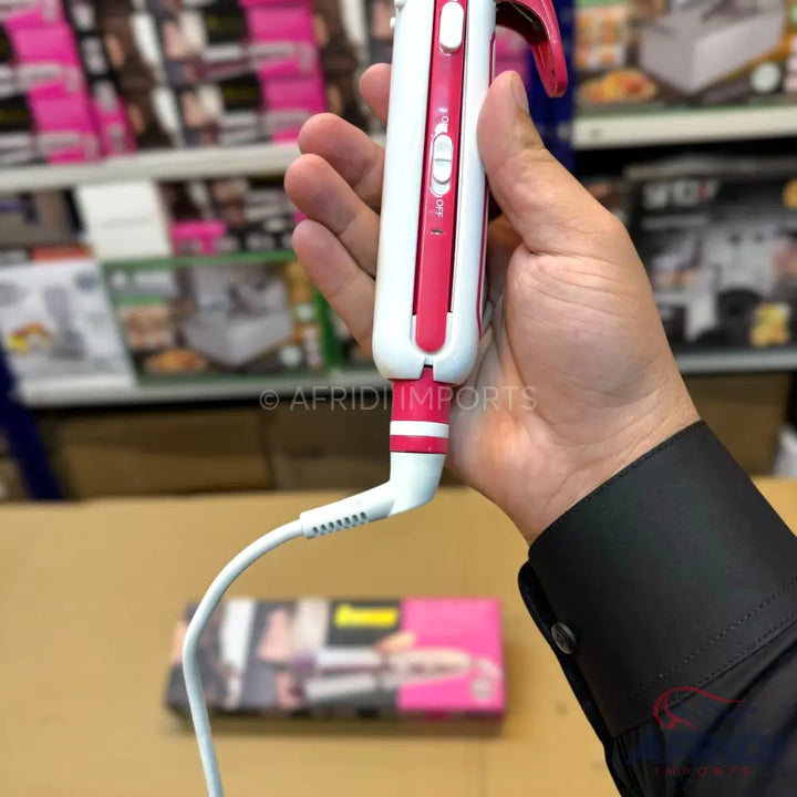 A white and pink hair curler with a power cord, held in a person’s hand.