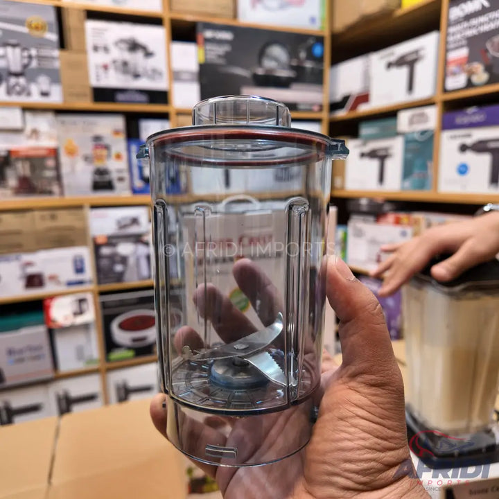 A clear plastic blender cup with an attached blade assembly.