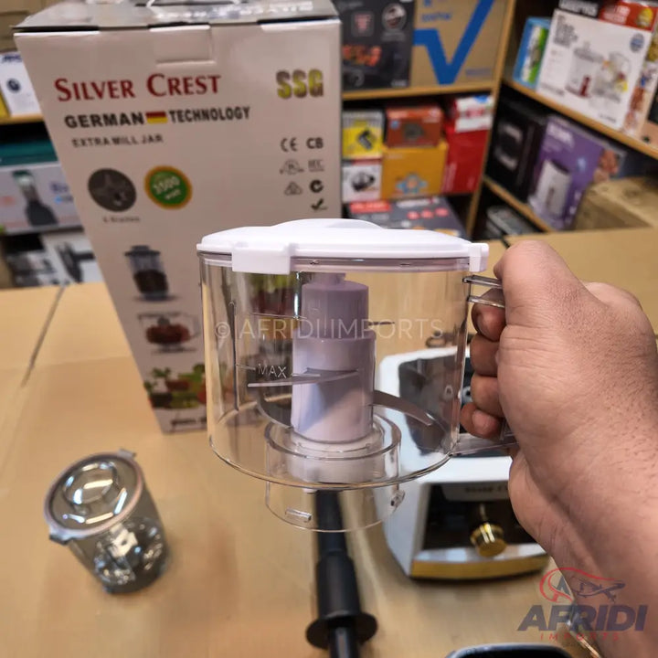 A clear plastic food chopper with a white lid and a handle, featuring a two-blade design inside and ’MAX’ fill line indicator.