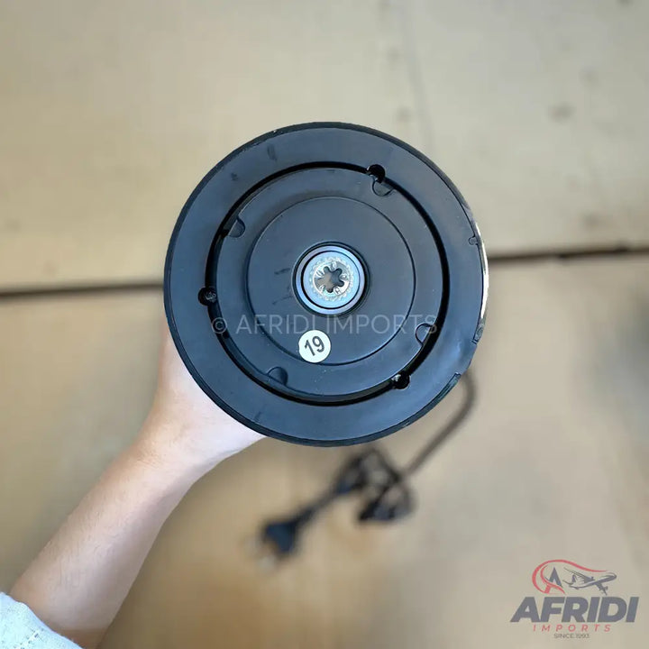 Black air conditioning compressor clutch plate with a central splined hole and a ’19’’ sticker.