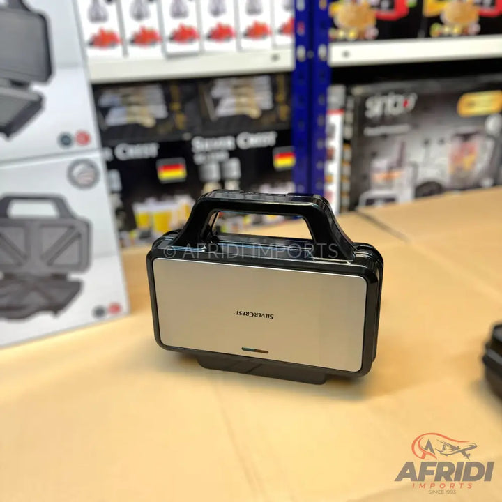 A closed, silver and black sandwich maker with a top handle.