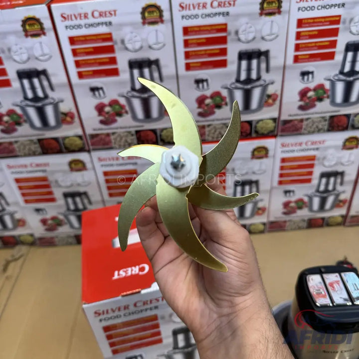 A six-bladed gold-colored food chopper attachment with a white plastic center.