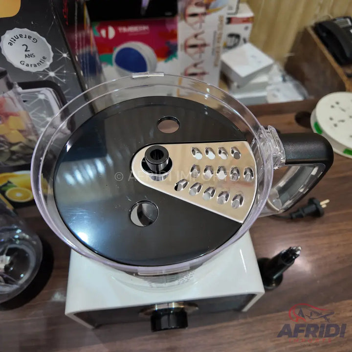 A food processor with a clear lid and a black and silver grating/slicing disk.