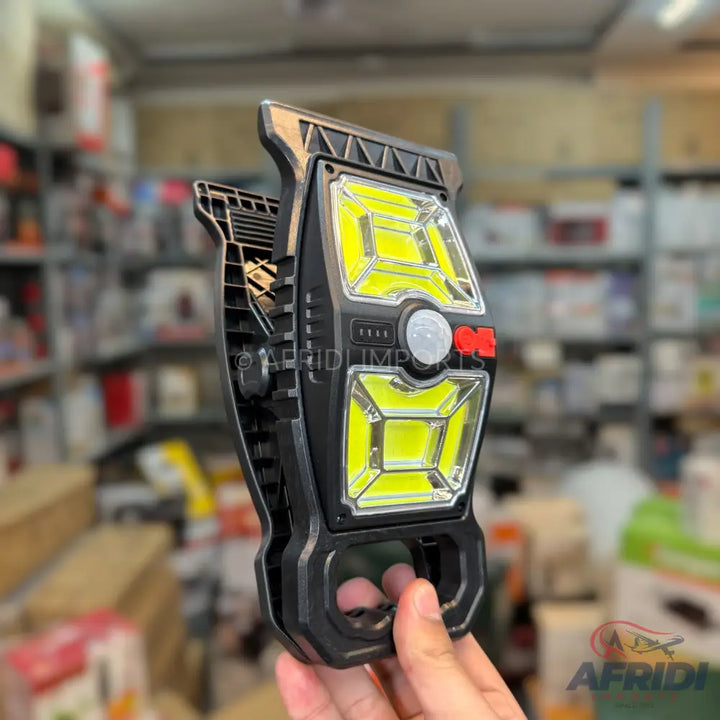 Black portable work light with bright yellow LED panels, a motion sensor, and a clip-on design.