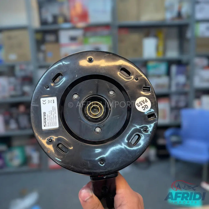 The base of a black electric kettle, held in a hand, with a central electrical connector and a label displaying specifications.