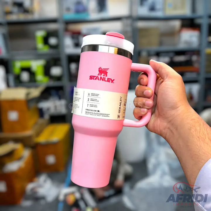 A pink Stanley travel mug with a handle and a white lid.