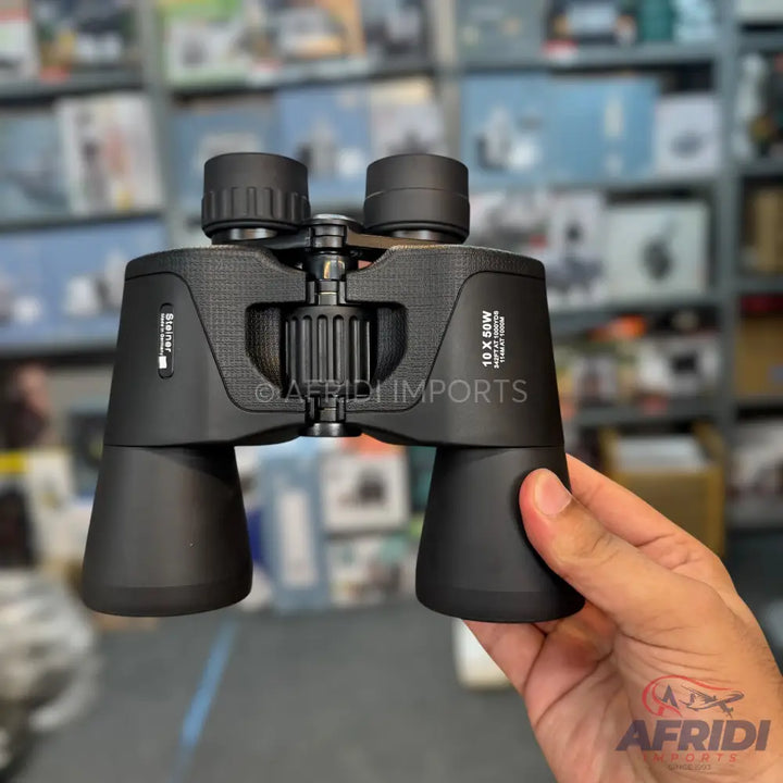Black binoculars with textured grip and adjustable focus, held in a hand.