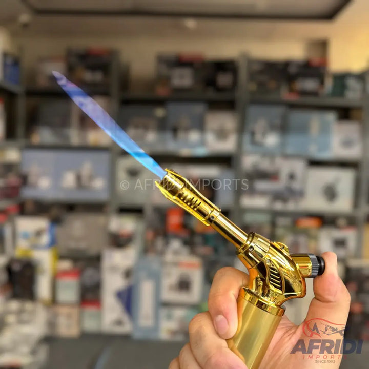 A gold-colored butane torch lighter with a blue flame.