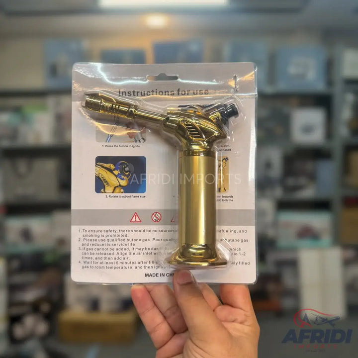 A gold-colored butane torch lighter in blister packaging.