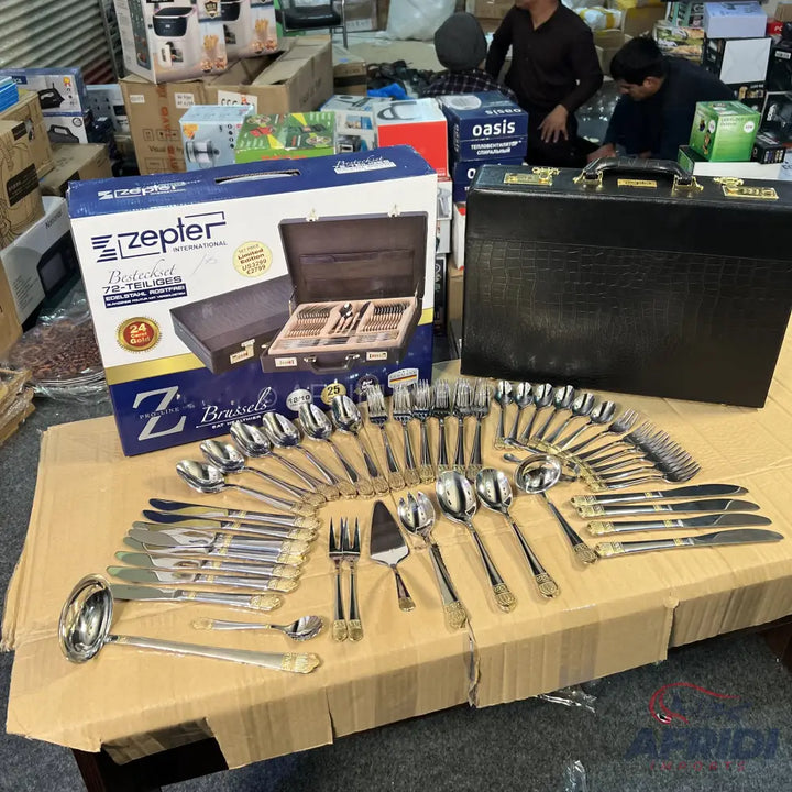 A complete stainless steel flatware set with gold accents, presented in a black carrying case and its original packaging.