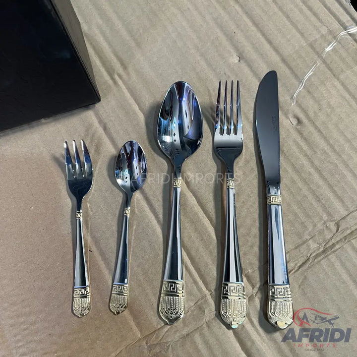 A five-piece set of silver-colored flatware with ornate gold-tone handles.