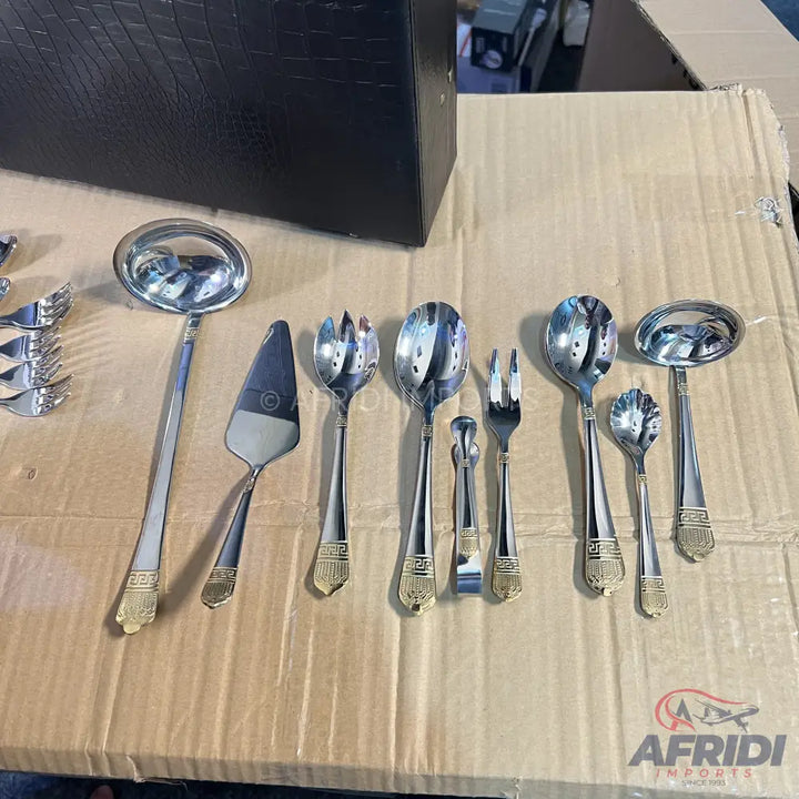 A set of polished stainless steel serving utensils with gold-toned, ornate handles.