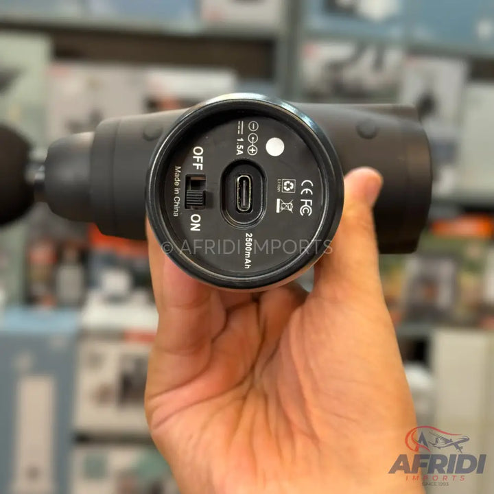 A black handheld massage gun with a USB-C charging port and an on/off switch.