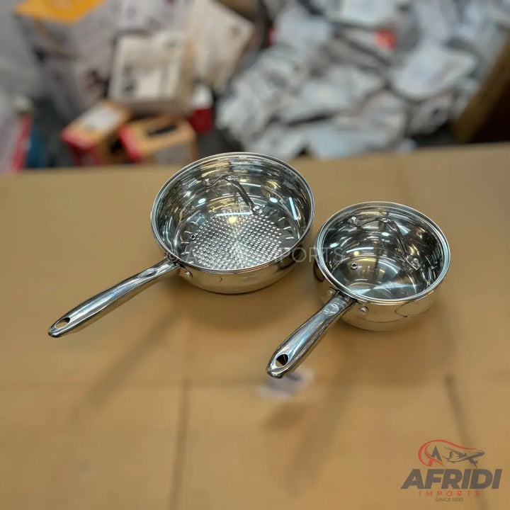 Two shiny stainless steel saucepans with long handles.