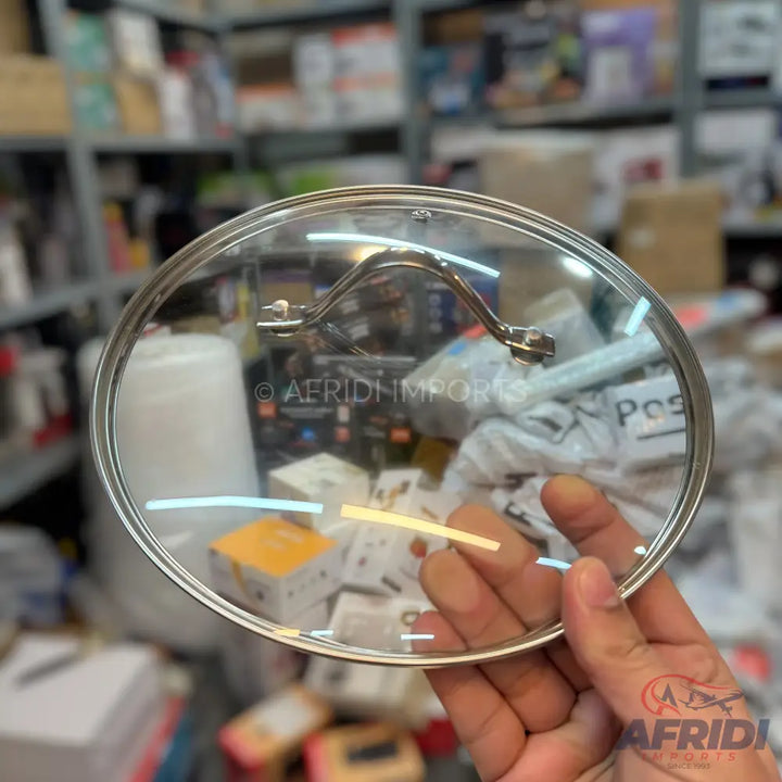 A clear glass pot lid with a metal rim and a curved metal handle.