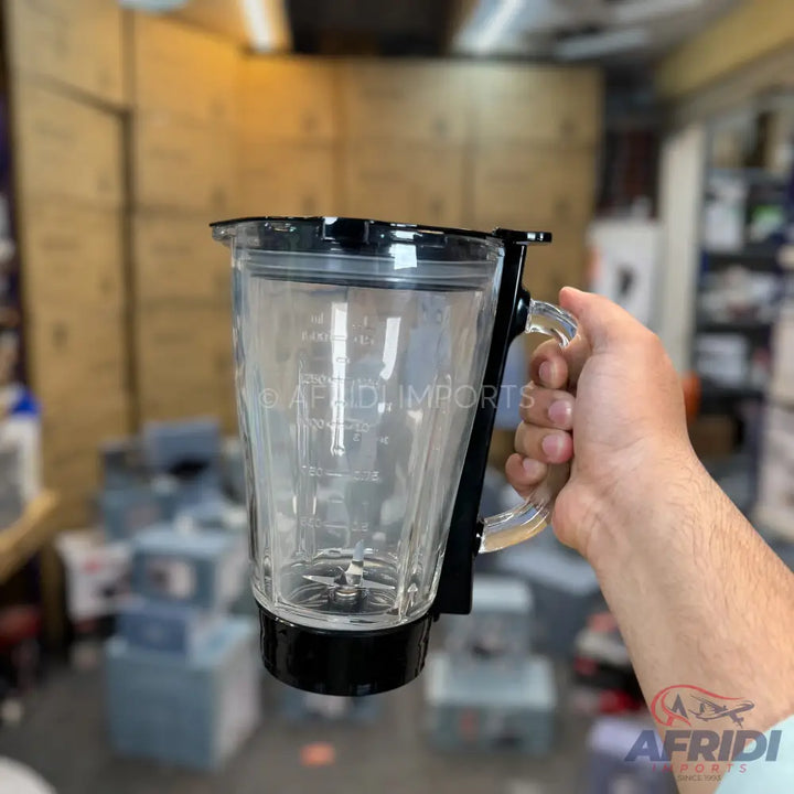 Clear glass blender jar with a black lid, handle, and base, featuring internal blades.