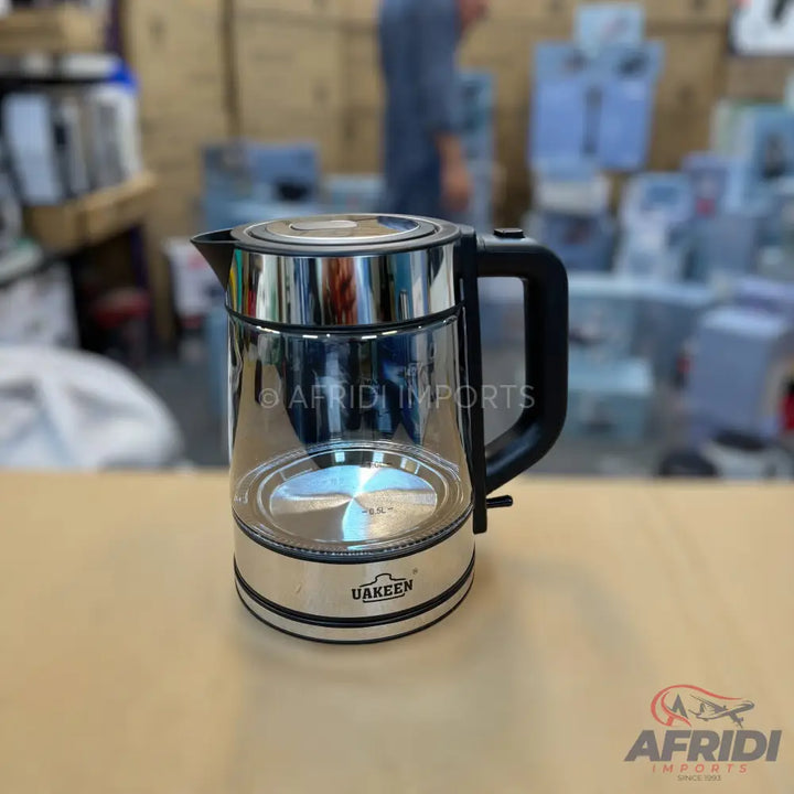 A glass and stainless steel electric tea kettle with a black handle.