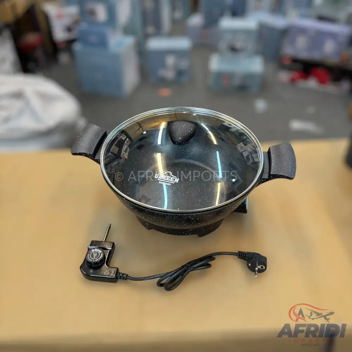 Black electric cooking pot with a glass lid and power cord.