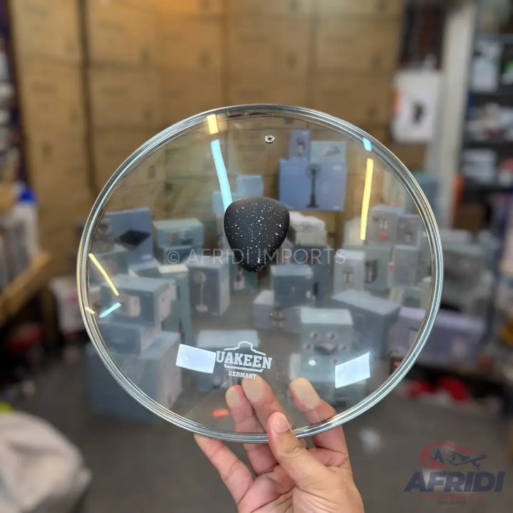 A clear glass pot lid with a black, speckled handle.