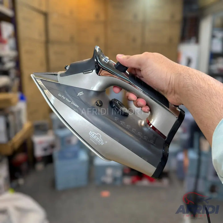 A person holding a grey and black steam iron with a metallic soleplate.