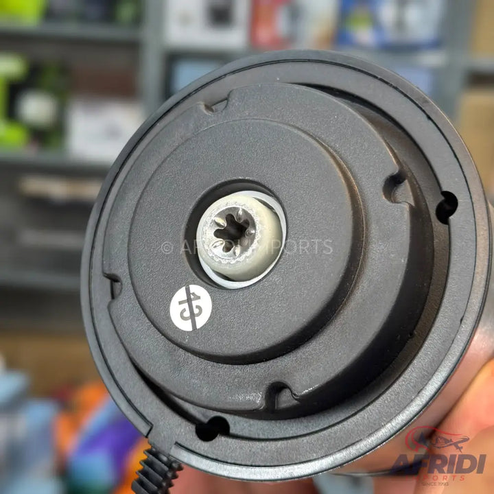 The bottom of a black electric appliance, revealing a star-shaped screw, a circular white symbol, and a coiled cord.