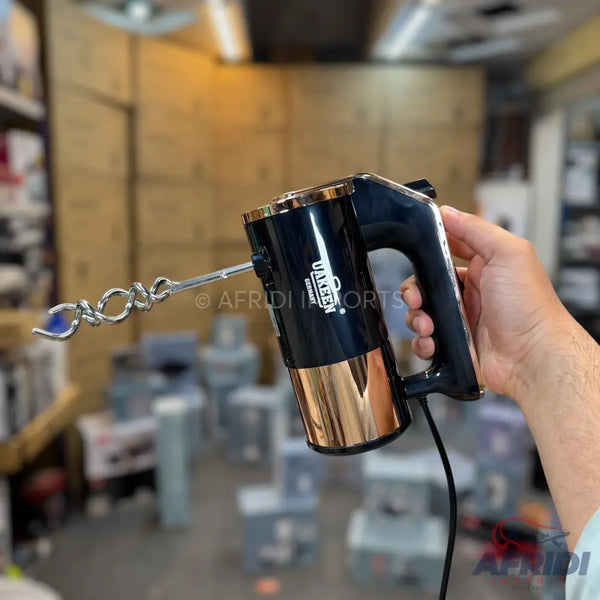 Black and gold electric hand mixer with a single whisk attachment.