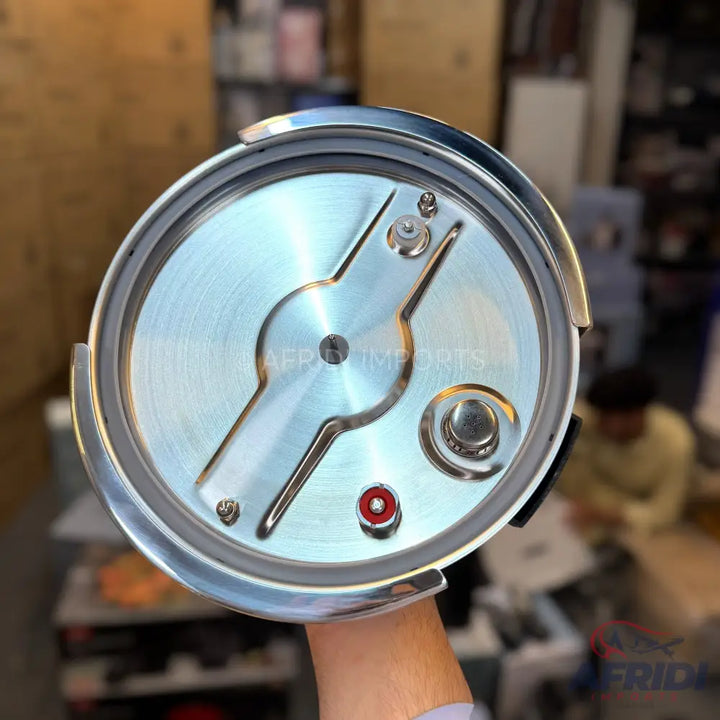 A polished metallic pressure cooker lid with a gasket, safety valve, and pressure regulator mechanism.