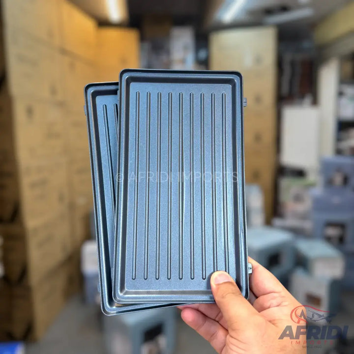 Two rectangular, ribbed, non-stick grill plates held by a hand.