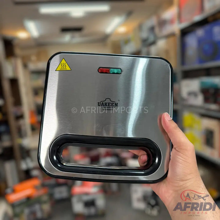 Stainless steel sandwich maker with a black handle and two indicator lights.
