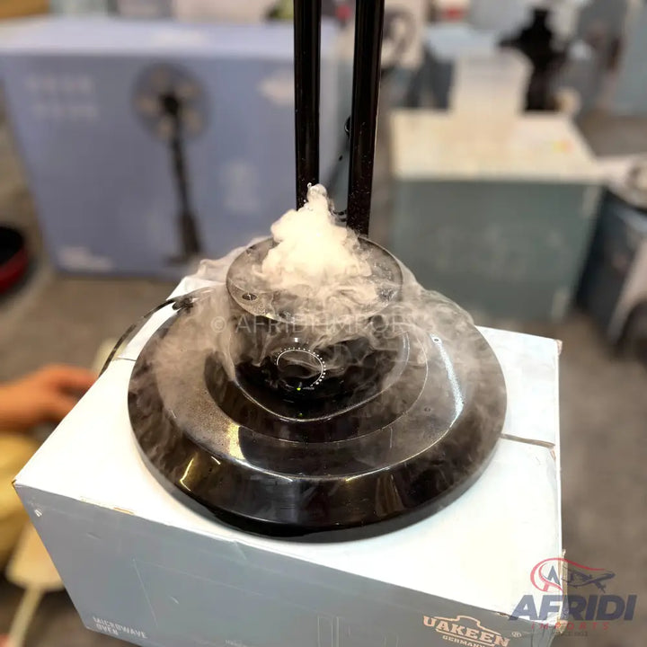 A black, multi-tiered humidifier or fog machine emitting a cloud of white mist.