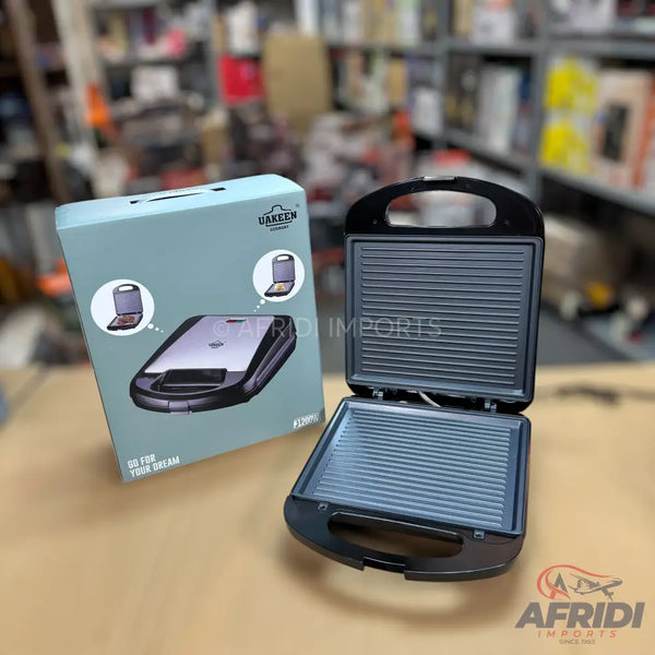 Black electric sandwich maker with ribbed cooking plates, shown open, alongside its light blue packaging.