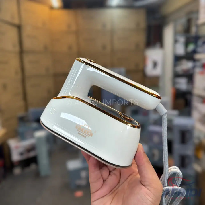 A white and gold handheld garment steamer with a power cord.