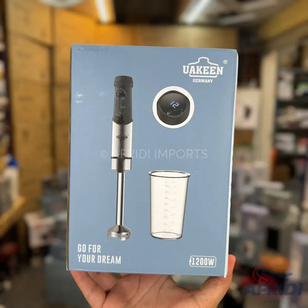 A ’Uakeen Germany’ branded hand blender with a 1200W motor, including a measuring cup and a digital display.