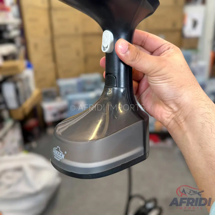 A handheld garment steamer with a gray and black body, a clear water tank, and a white power button.