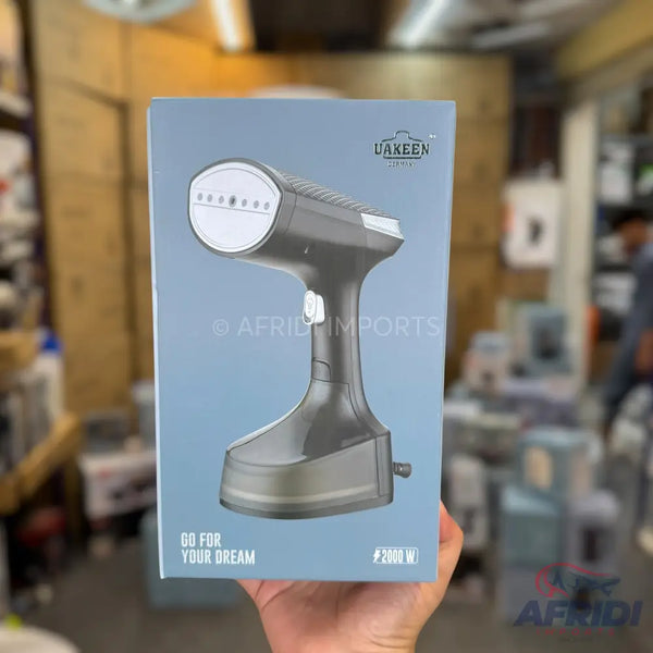 Boxed handheld garment steamer with a dark grey body and white steaming plate.
