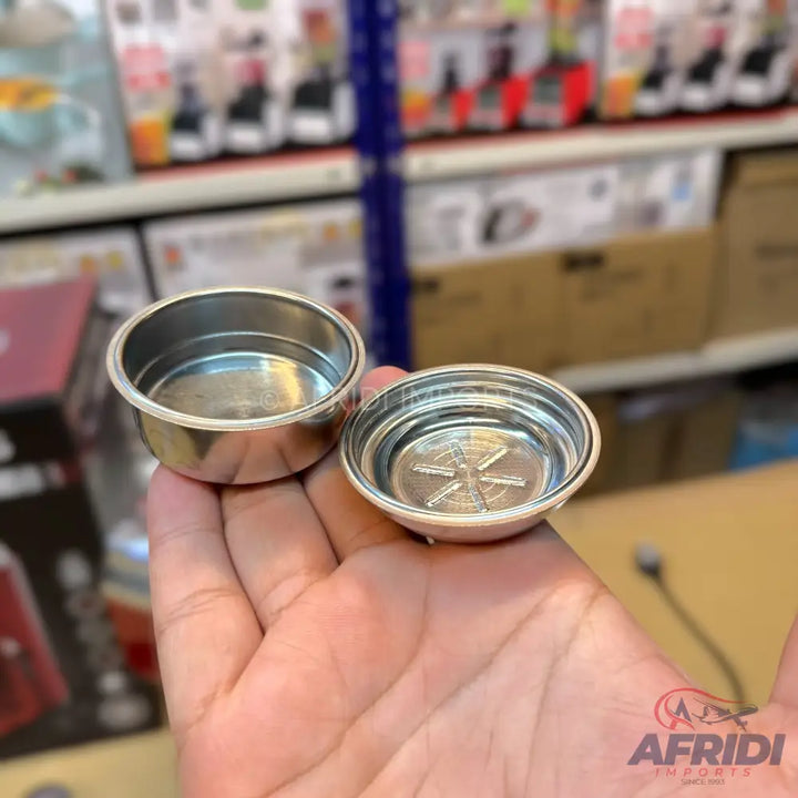 Two stainless steel espresso filter baskets, one with a raised star pattern on the bottom.