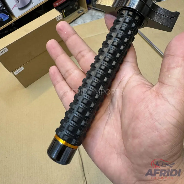 A black, textured, metallic baton with a golden ring near the base.