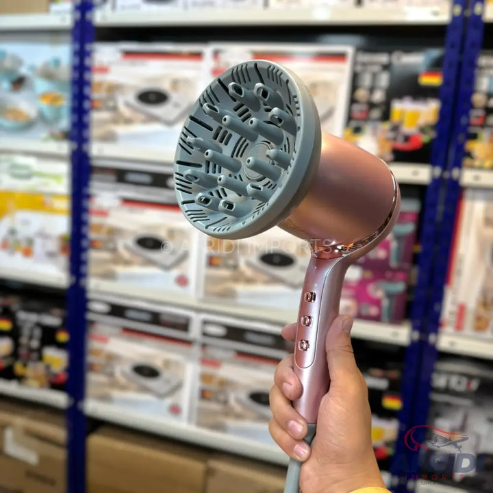 Rose gold hair dryer with a gray diffuser attachment, held in a hand.